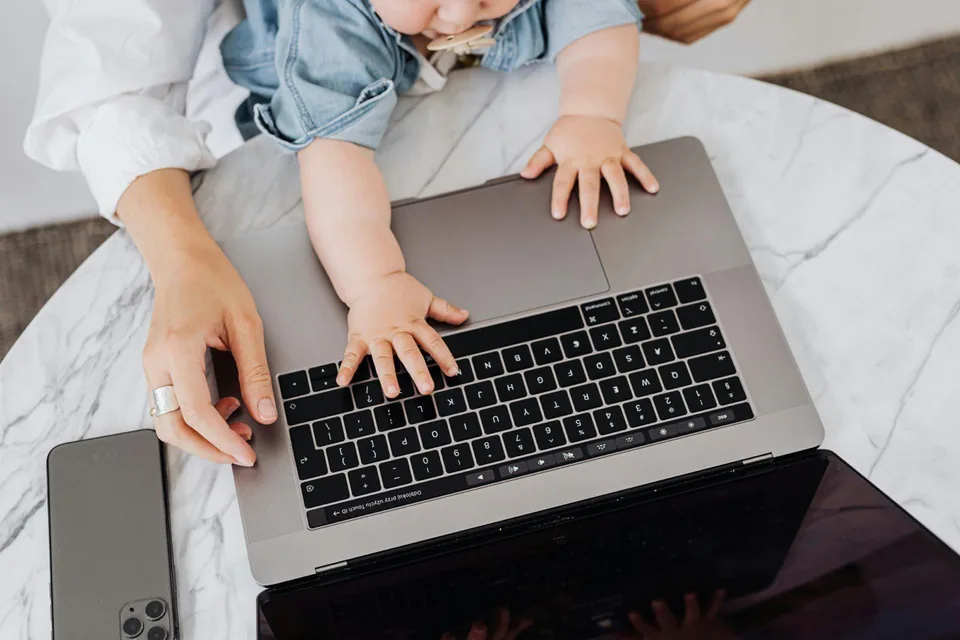 Child reaching for a laptop keyboard beside a parent